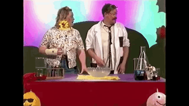 a man and a woman are standing next to each other at a table with a bowl of liquid .