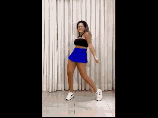 a woman in a blue skirt and black top is dancing in a living room .