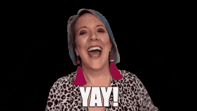 a woman wearing a leopard print shirt and pink earrings is saying yay