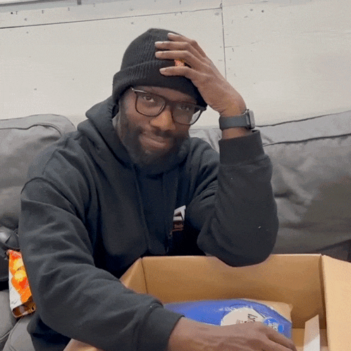a man wearing a beanie and glasses is sitting on a couch with his hand on his head