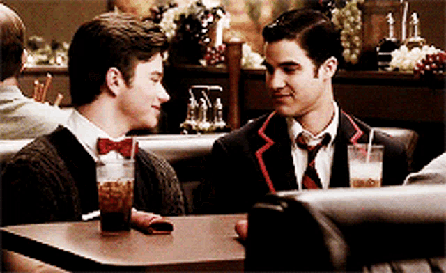 two men are sitting at a table in a diner with drinks