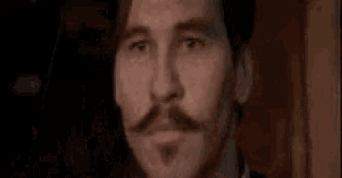 a close up of a man 's face with a mustache in a dark room .