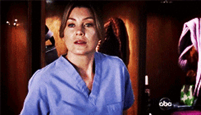 a woman in a blue scrub top is standing in front of a abc sign