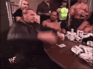 a group of men are sitting around a table with a sign that says wwe on it .