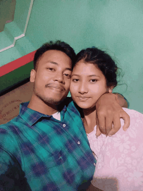 a man and a woman pose for a picture with a green wall behind them