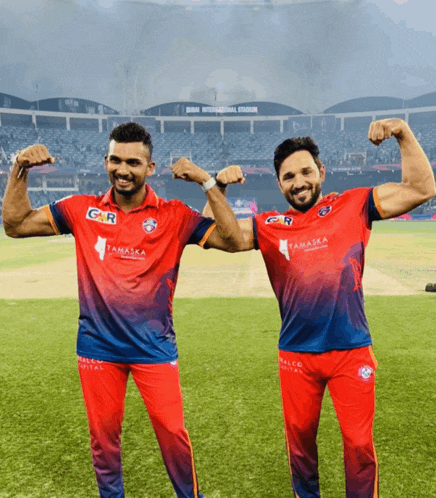 two men are posing for a picture on a field and one of their shirts says tamasha on it