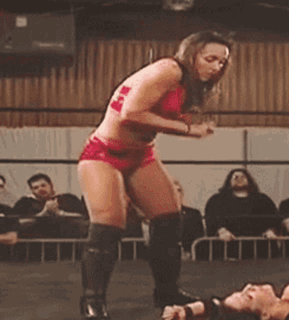 a woman in a red top and shorts is standing in a wrestling ring .