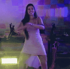 a woman in a white dress is dancing in front of a purple wall