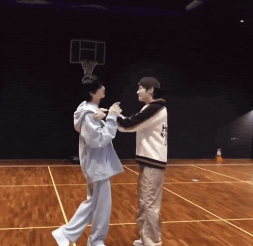 two men are dancing on a basketball court with a basketball hoop behind them
