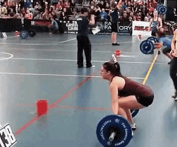 a woman is squatting down to lift a barbell in a gym while a crowd watches .