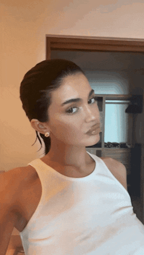 a woman wearing a white tank top takes a selfie