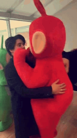 a man in a suit hugging a teletubbies costume