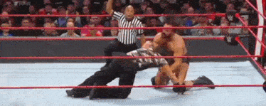 two men are wrestling in a wrestling ring with a referee in the background .
