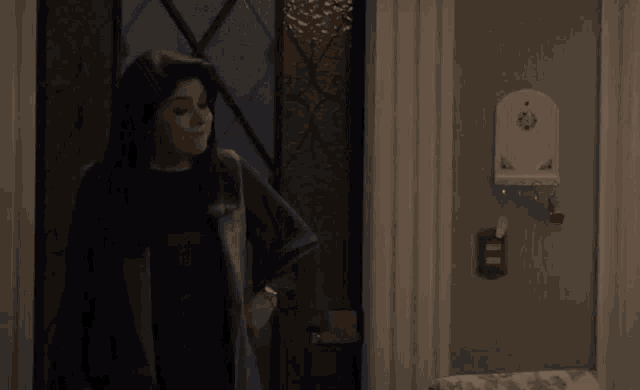 a woman standing in a living room with a lamp and a key holder on the wall