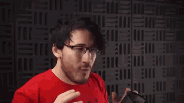 a man with glasses and a red shirt is making a funny face in front of a wall .