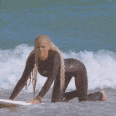 a woman in a wet suit is kneeling on a surfboard