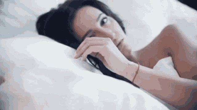 a woman is laying on a bed with white sheets and looking at the camera .