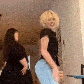 two women are dancing together in a room and one of them is wearing a black shirt and blue jeans .