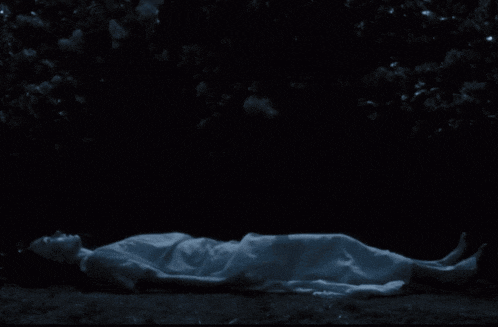 a woman in a white dress is laying in the dark