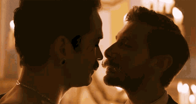 a man with a mustache is kissing another man on the nose