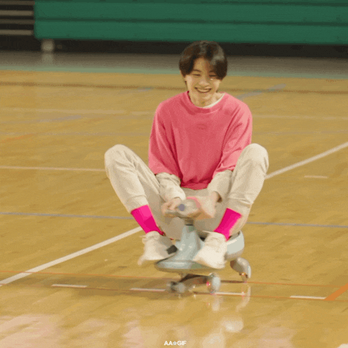 a young boy in a pink shirt is sitting on a skateboard
