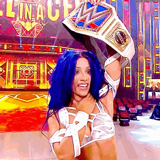 a woman with blue hair is holding a wrestling championship belt over her head