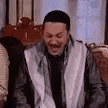 a man is sitting on a couch and laughing .