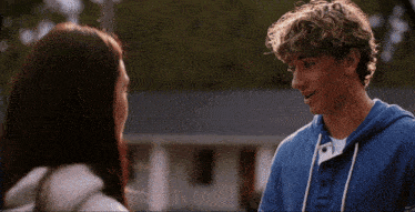 a boy and a girl are looking at each other and the boy is wearing a blue hoodie