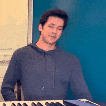 a young man in a hoodie is playing a keyboard