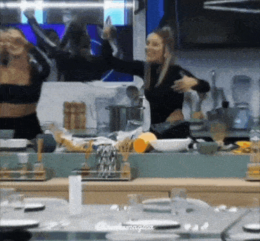 two women are dancing in a kitchen in front of a large mirror .