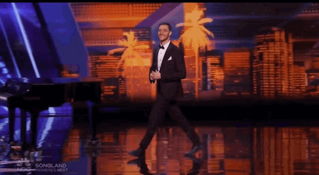 a man in a tuxedo stands on a stage in front of a piano and palm trees