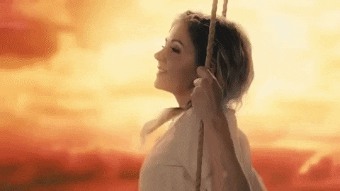 a woman is sitting on a swing at sunset and smiling .