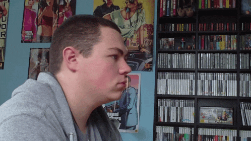 a man stands in front of a grand theft auto poster on the wall