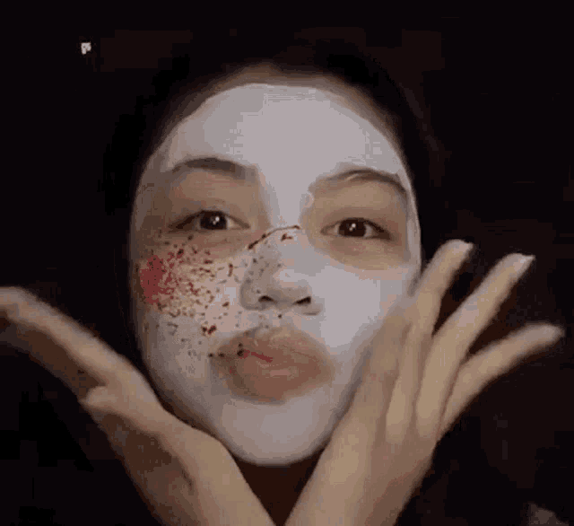 a woman is wearing a white face mask with blood spots on her face .