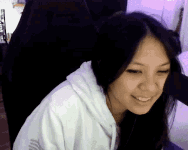 a woman in a white hoodie is sitting in a gaming chair and smiling