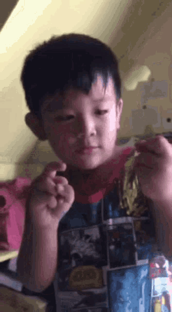 a young boy in a superhero shirt is holding a piece of paper in his hands .