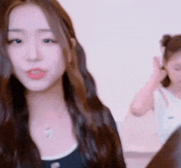 a close up of a woman with long hair looking at the camera with another woman in the background .