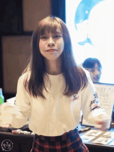 a girl wearing a plaid skirt and a white shirt with the letter t on the sleeves