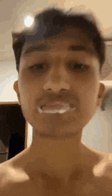 a man without a shirt is taking a selfie with his mouth open and white liquid coming out of it .