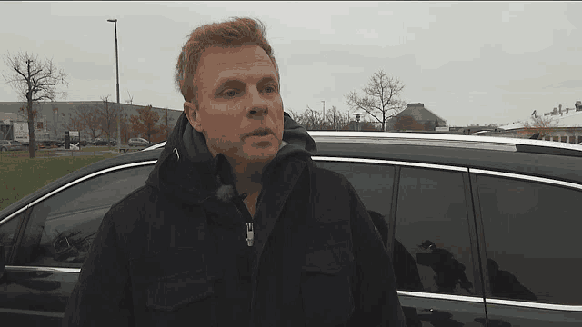 a man in a black jacket is standing next to a black car