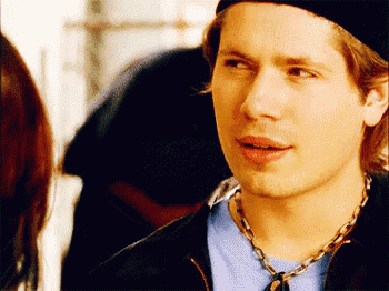 a man wearing a black hat and a necklace looks at a woman