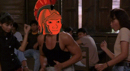 a man wearing a spartan helmet is dancing in front of a group of people in a room .