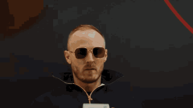 a bald man wearing sunglasses and a blue jacket looks at something
