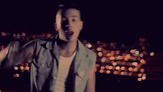 a man in a denim vest is singing into a microphone in the dark