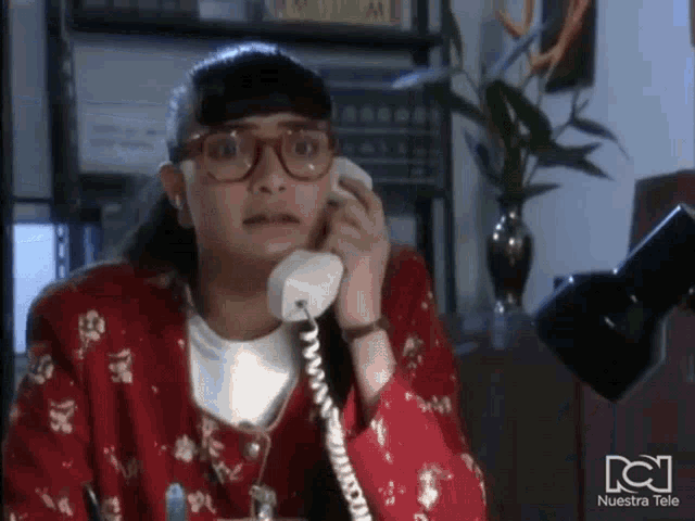 a woman wearing glasses is talking on a phone with nuestra tele written on the bottom