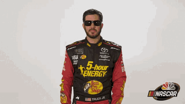 a man wearing a 5 hour energy shirt is standing in front of a nascar logo