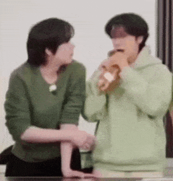 a couple of men are standing next to each other in a room . one of the men is drinking from a cup .
