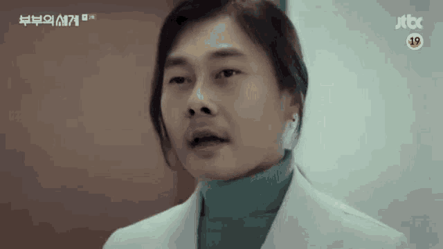 a man wearing a white coat and a green turtleneck is talking to someone .