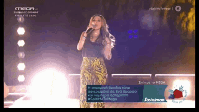 a woman singing into a microphone on a stage in front of a mega logo