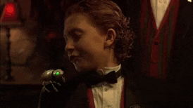 a young boy in a tuxedo and bow tie is talking into a microphone .